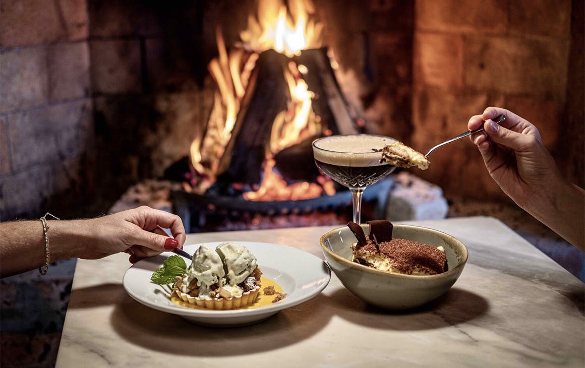 A couple dig into some delicious looking fare by the fireplace at Fenice restaurant on Waiheke Island.
