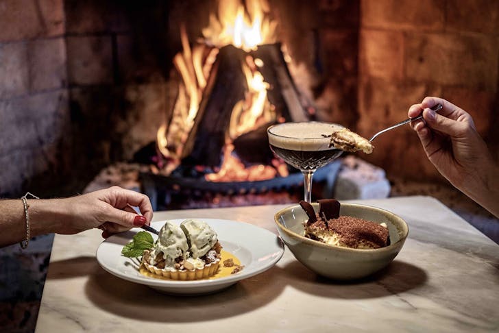 A couple dig into some delicious looking fare by the fireplace at Fenice restaurant on Waiheke Island.