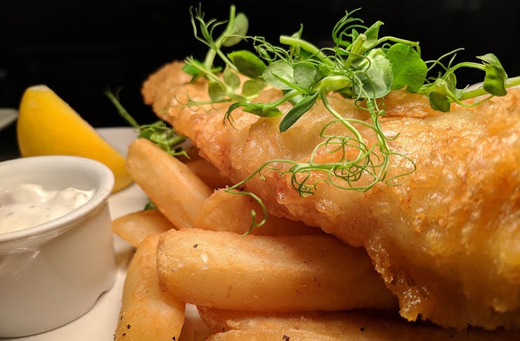 Fish and chips sit on a plate with a wedge of lemon and tartare sauce on the side.