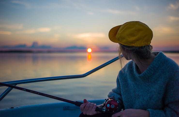 A woman looks at the horizon as she fishes off a boat.