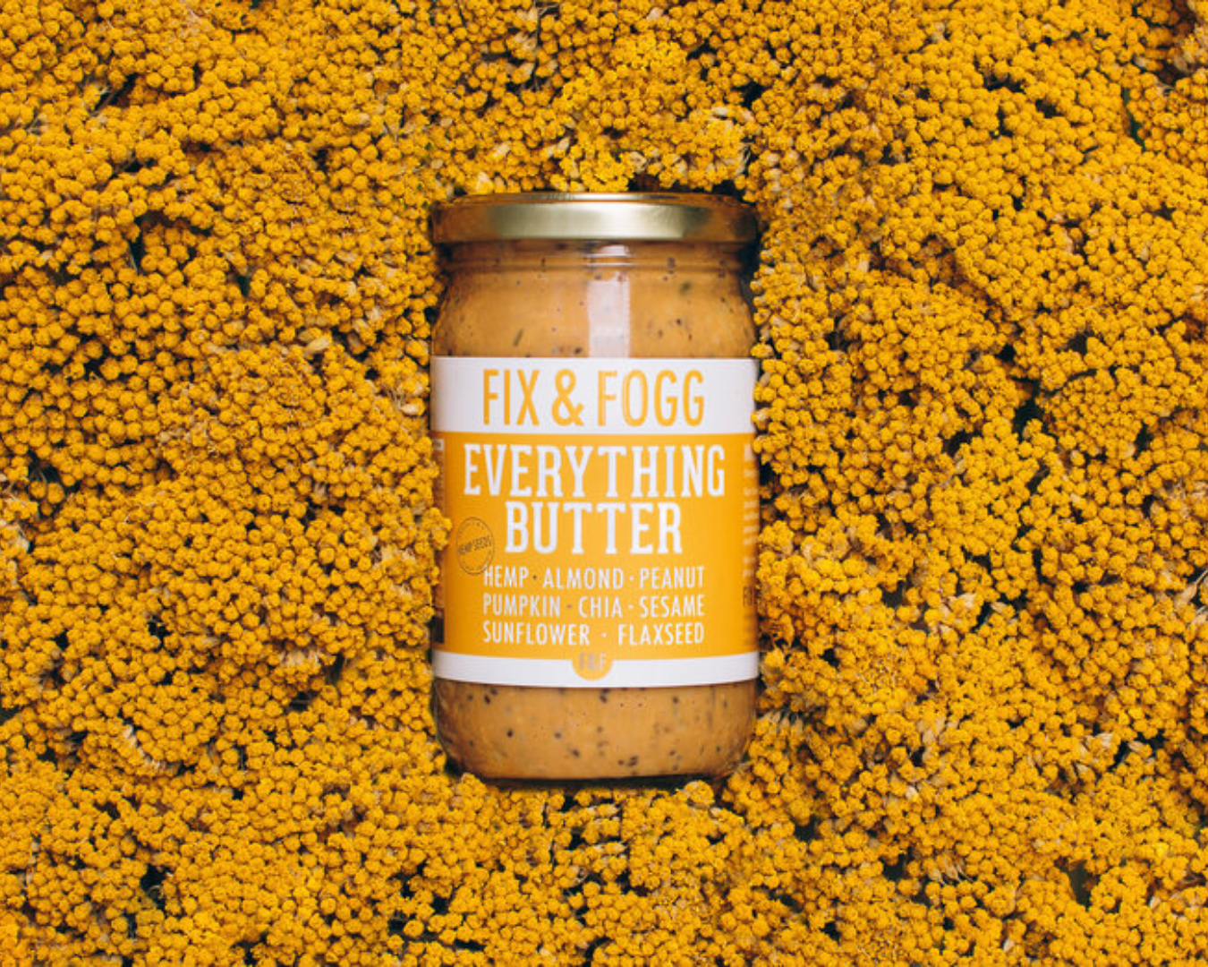 A jar of Fix & Fogg's Everything Butter stands out against a background of yellow flowers