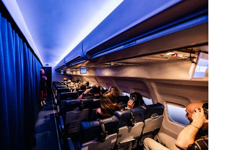 'Passengers' in the Darkfield experience 'FLIGHT' seated in a mock passenger airplane put headphones on.