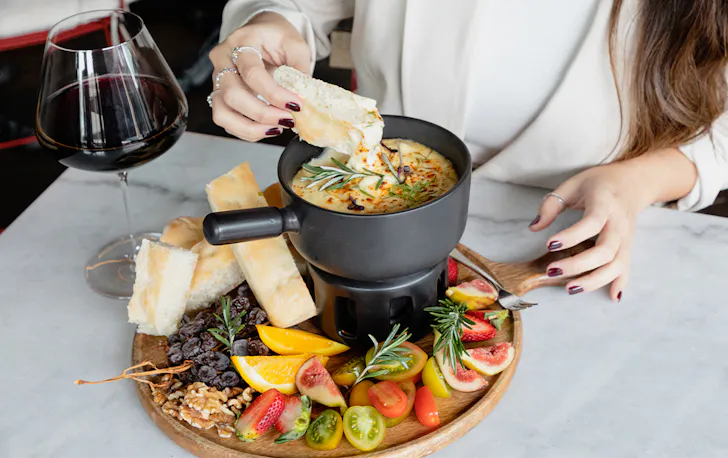 a person dipping focaccia into cheese fondue