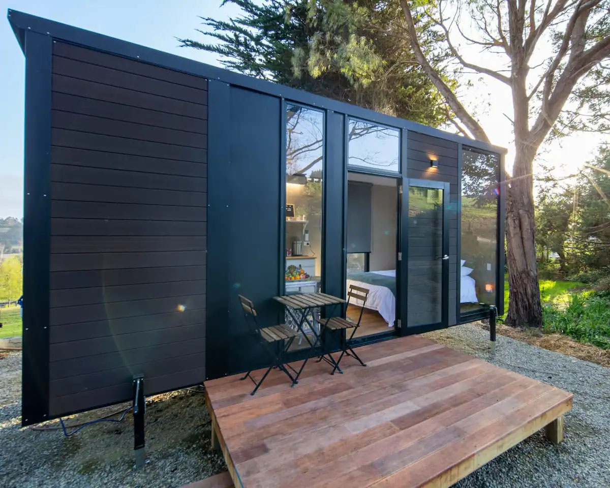 Tiny home nestled next to the woods in North Otago, with a small front porch and a coffee table for two.
