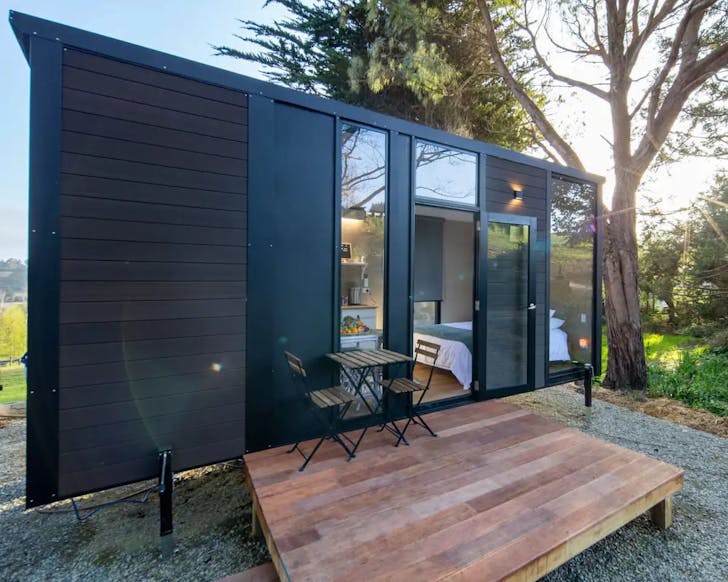 Tiny home nestled next to the woods in North Otago, with a small front porch and a coffee table for two.