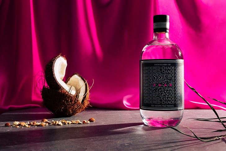 A bottle of Four Pillars gin next to a coconut and in front of a pink silk cloth.
