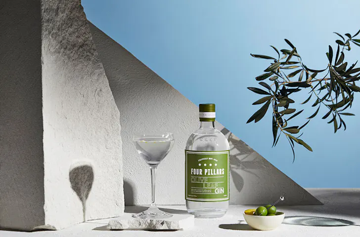 A stylised photo of Four Pillars Olive Leaf gin, featuring a martini and a bowl of olives. 