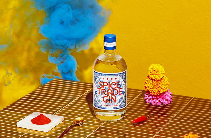 A bottle of colourful gin next to spices and blue smoke.