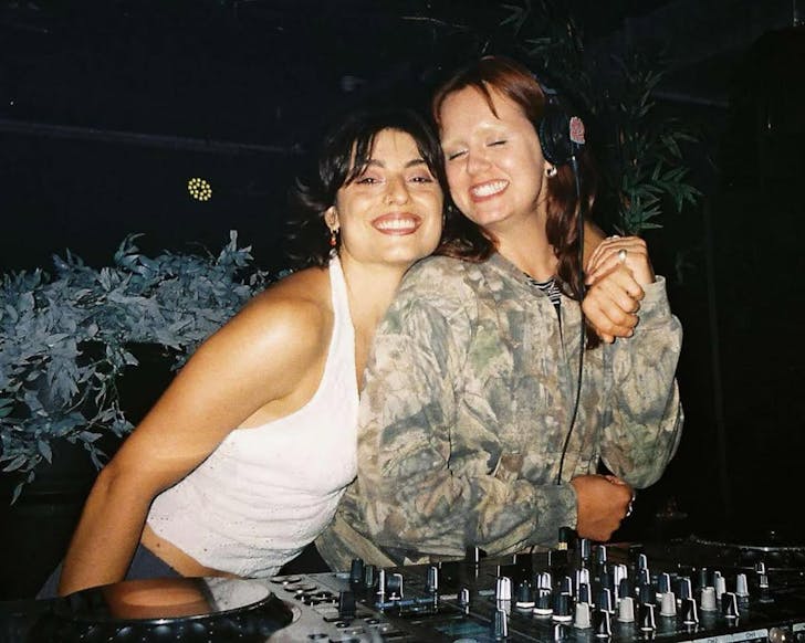 DJ's Foxtrot and Madam X embrace while posing for a photo above a set of decks.