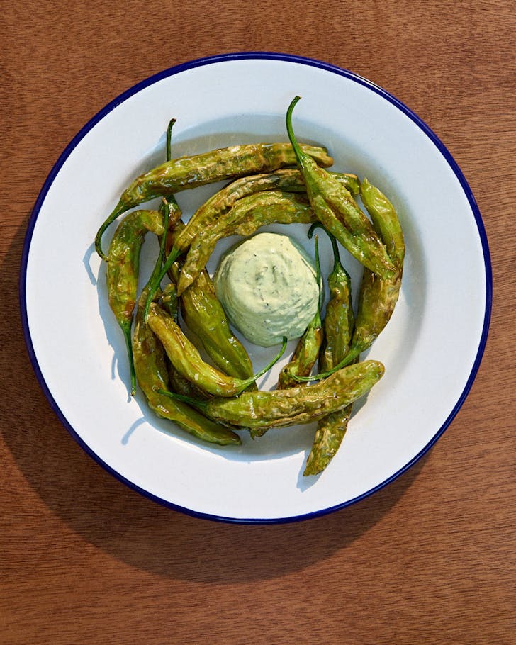 A plate of fried green shishito peppers with basil and feta whip. 