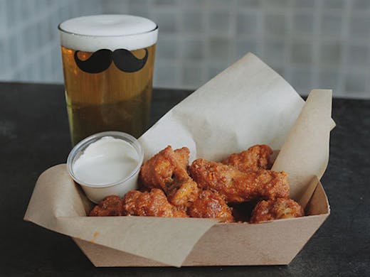 A box of wings and a beer glass with a moustache on it 