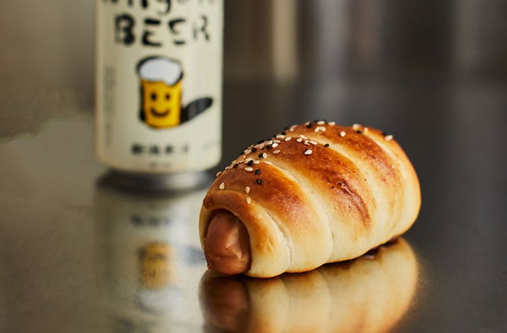A Japanese-style sausage roll on a surface with a can of Japanese beer.