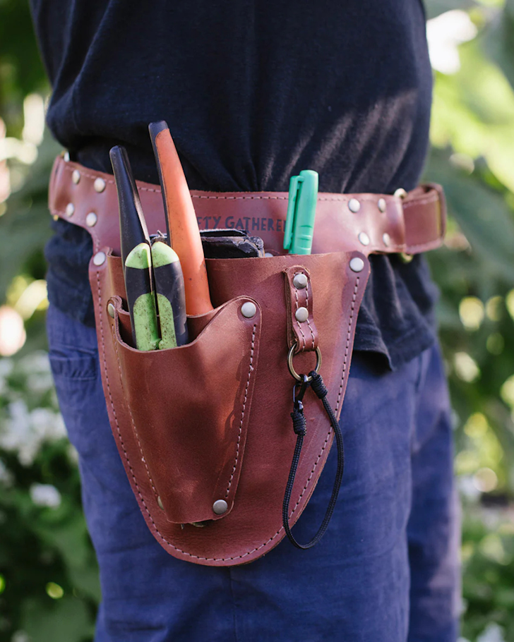 A close-up of someone wearing a leather garden belt full of gardening tools.