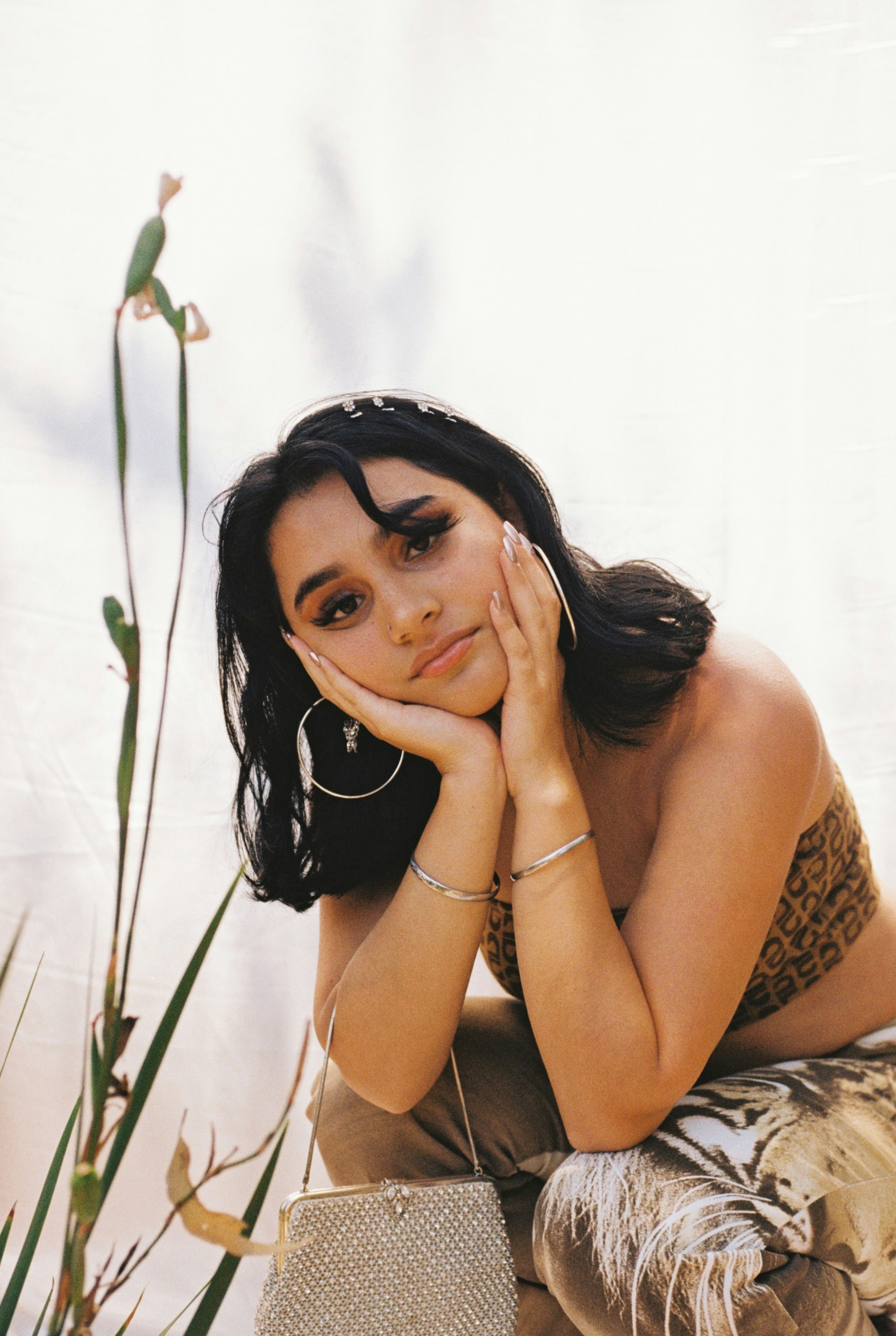 A girl sitting with her head resting in her hands looking towards the camera.