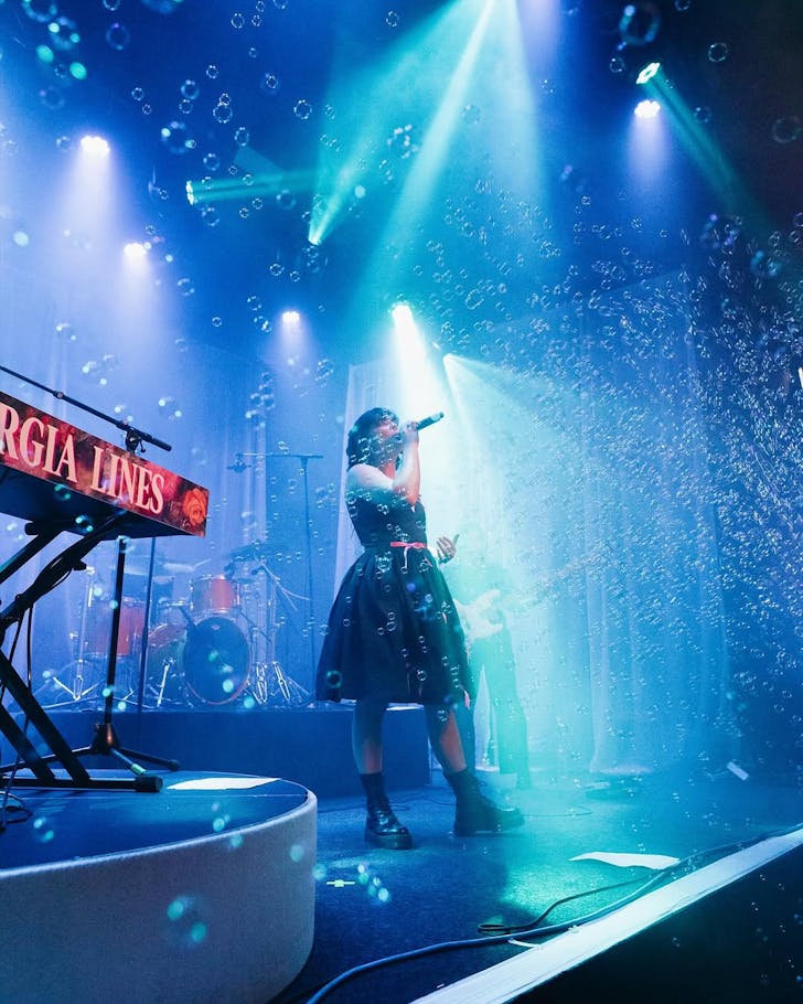 The brilliant Georgia Lines performs on a blue-lighted stage as bubbles surround her.