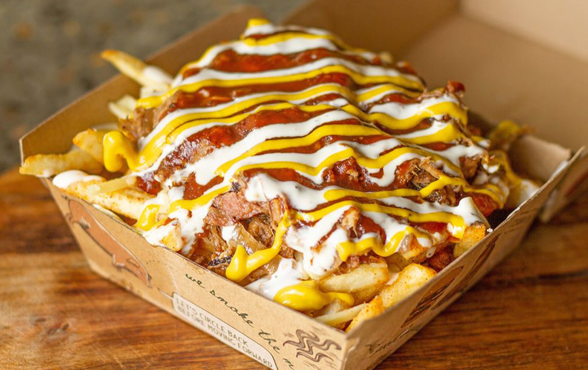A box of fries topped with mustard, ketchup and meats