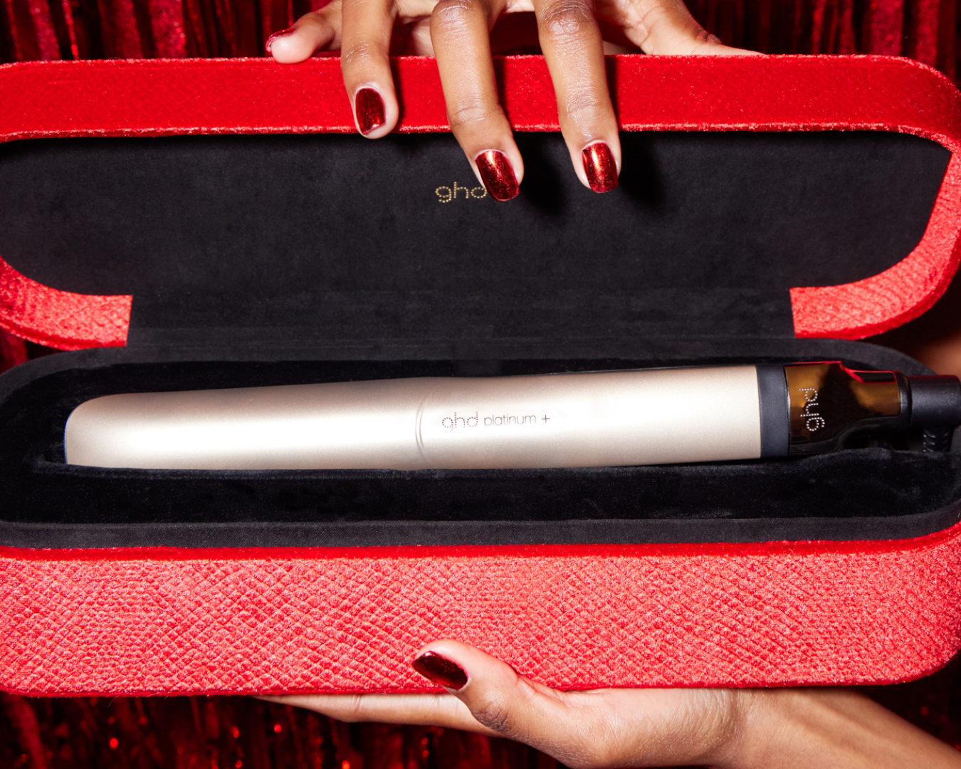 Hands holding a red velvet case which is housing a champagne gold ghd hair straightener.