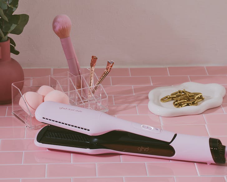 Pink ghd straighteners on a table with other pink bits. 