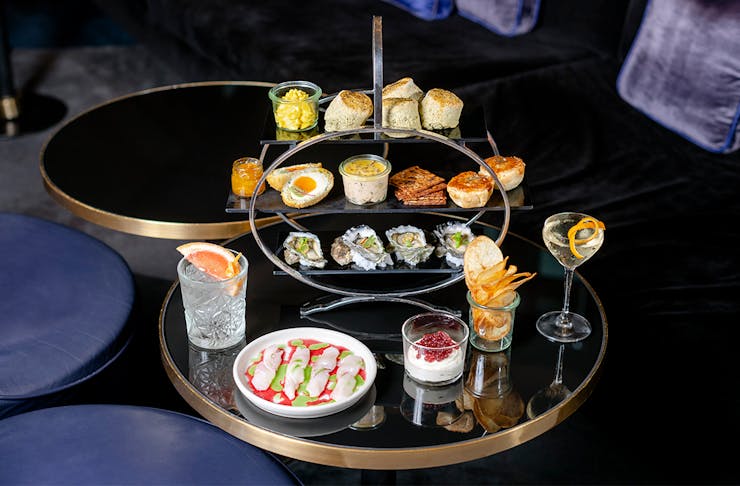 a tray filled with high tea bites with cocktails next to it