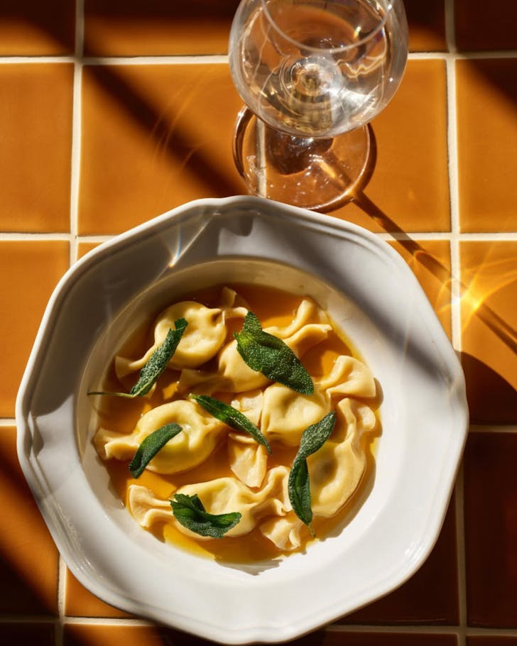 Gina pasta bar barangaroo, a house-made pasta dish with ravioli and sage is set on a table accompanied by a glass of white wine 