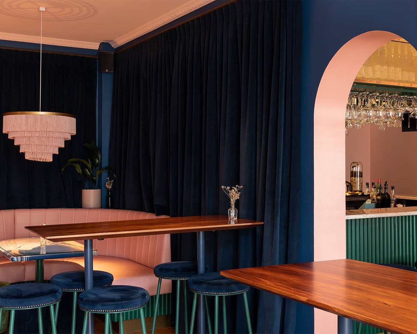 The sumptuous interior at Gin Gin shows pretty pastel pink booth seating with blue velvet curtains.