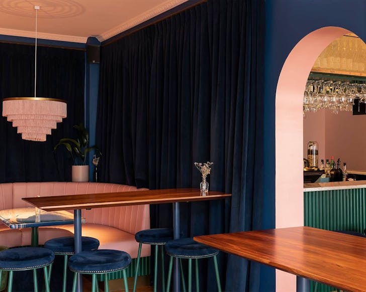 The sumptuous interior at Gin Gin shows pretty pastel pink booth seating with blue velvet curtains.