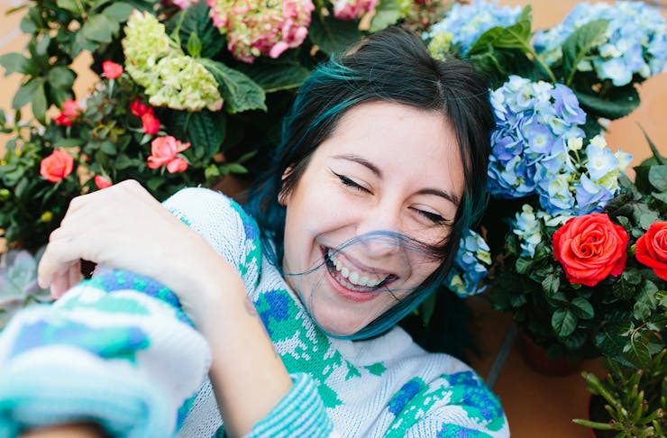 A girl wearing a blue jumper relaxes amongst some flowers and looks like she's having a great time.