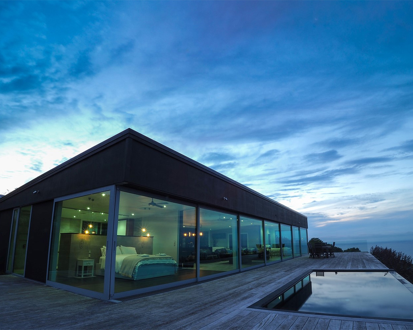 The outside of the lovely glasshouse, showing an infinity pool to the right under a sky at dusk.