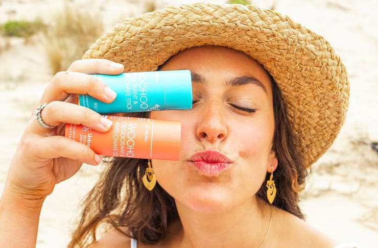 A woman wearing a straw hat holds two natural deodorants from Wahoo. 