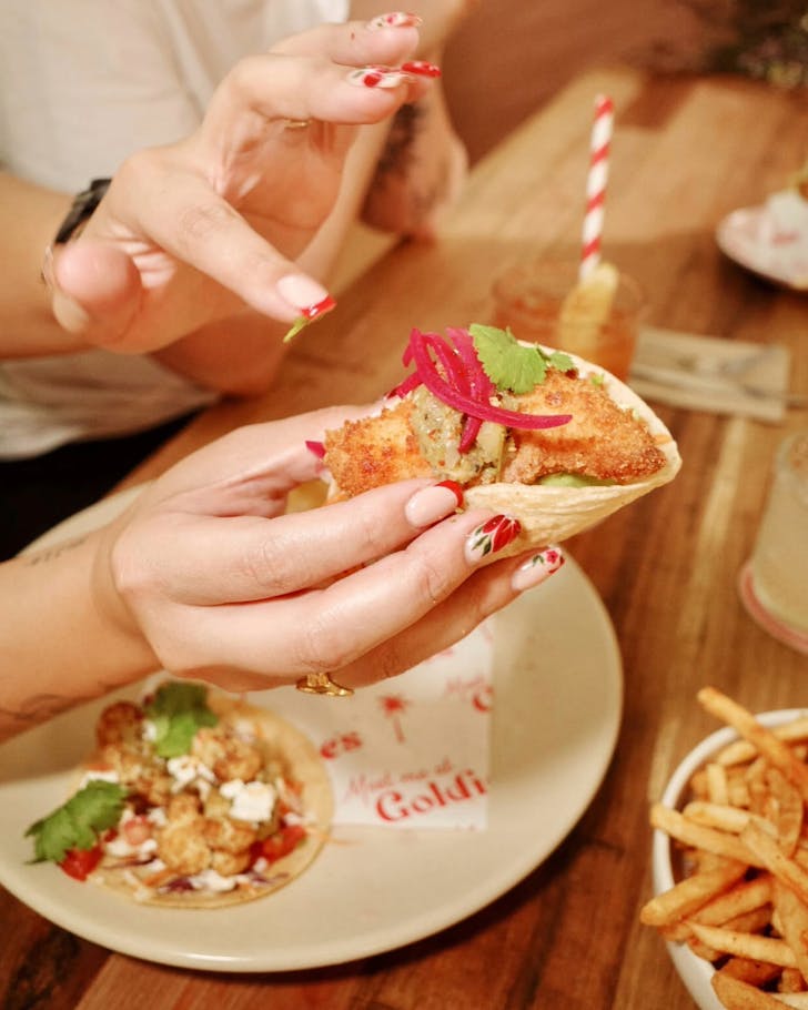 A close up image of a lady's hands grabbing one taco from a plate of taco's to eat.