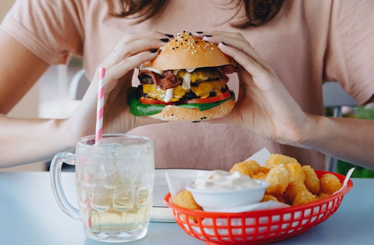 A woman holding a burger with her two handsâthe burger is filled with lettuce, tomato, bacon, egg and cheese. The burger is served at Good Times Milk Bar, a cafe dishing up some of the best breakfasts in Melbourne