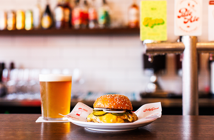 A single burger plated up on a bar with a beer next to it—one of the best burgers in Melbourne