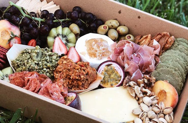 A gourmet picnic platter box, filled with cheeses, crackers, fruit, meats and nuts.