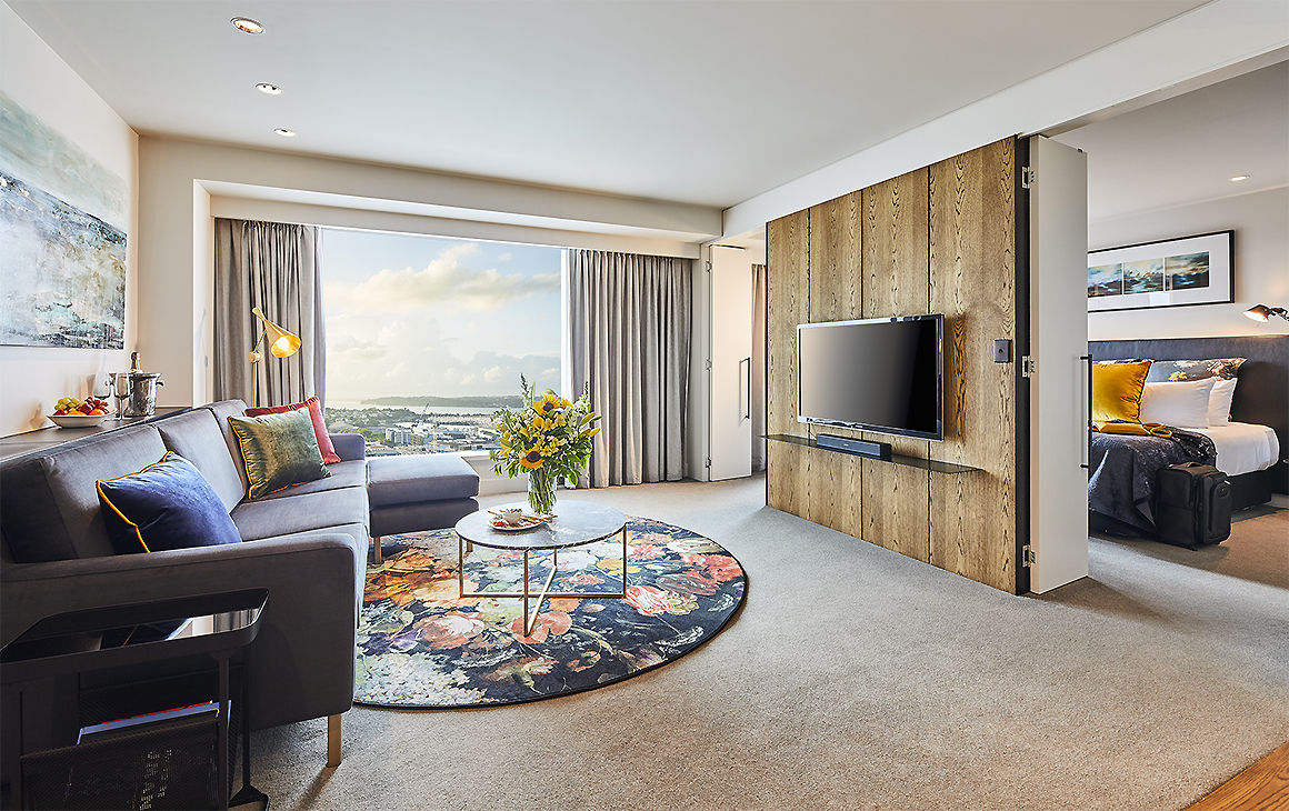 A room at The Grand By SkyCity Hotel showing a comfortable living area with a luxury bedroom in the background.