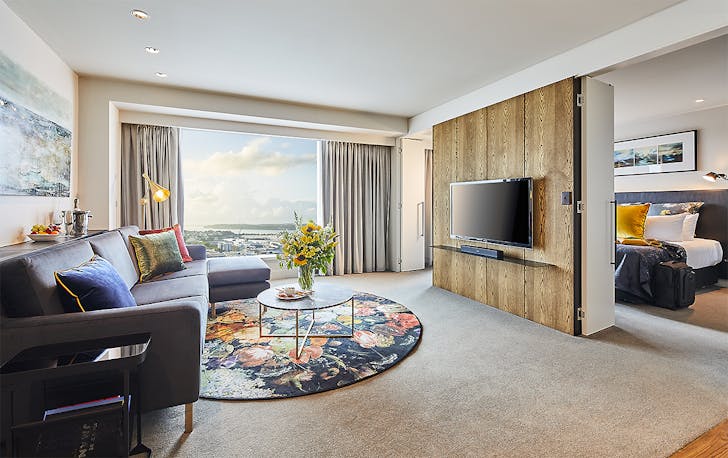 A room at The Grand By SkyCity Hotel showing a comfortable living area with a luxury bedroom in the background.