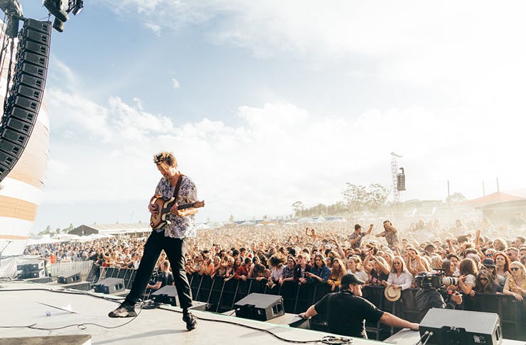 A man playing guitar on a stage at a festival.