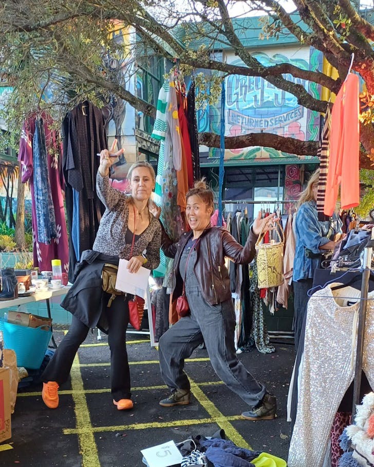 Two people pose beneath a tree and in front of the eclectic Grey Lynn Car Boot Market.