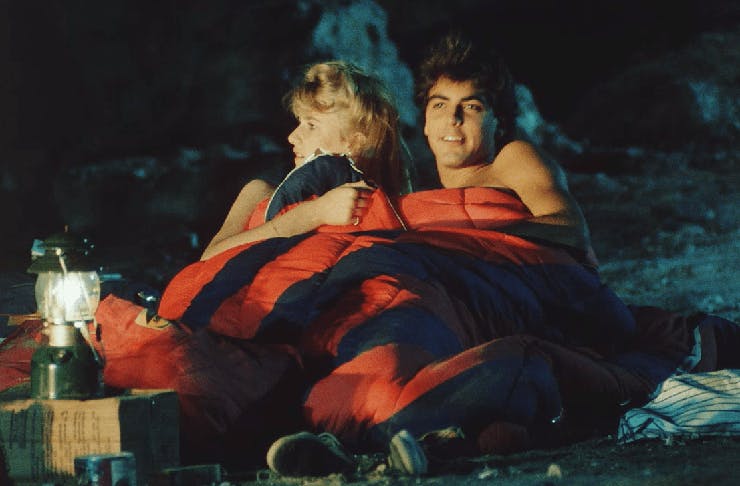 A young George Clooney and Laura Dern laying in a sleeping bag at night, on the set of 'Grizzly 2. Revenge'.