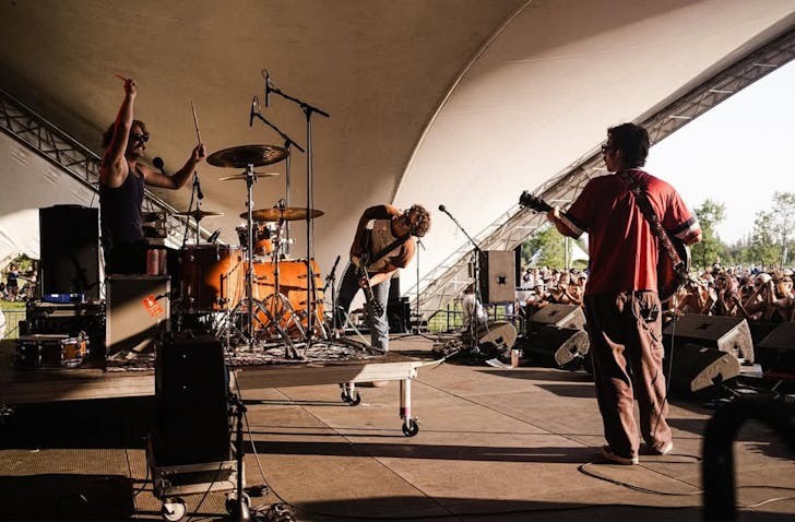 The Grogans perform on a stage at an outdoor venue during the late-afternoon sun hours.