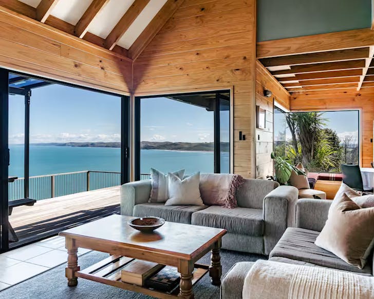 The lounge and outdoor deck area of a large, comfortable-looking bach above the Raglan coastline.