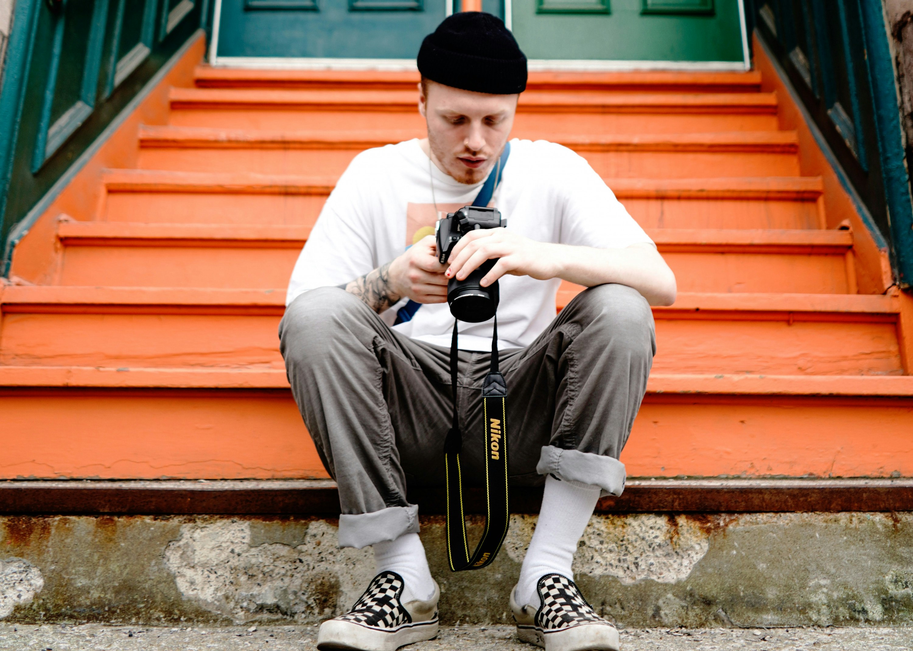 A man sits on orange steps while looking at his SLR camera. 