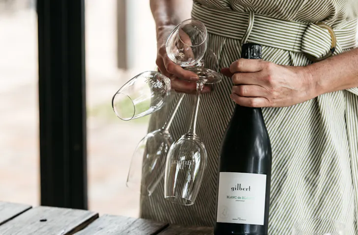 A person clutching a bottle of sparkling wine and champagne flutes 
