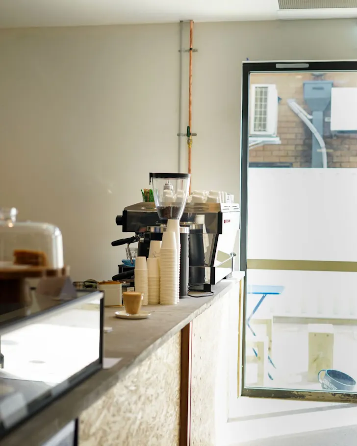 Minimalist coffee bar with an espresso machine, takeaway coffee cups and a freshly made coffee on the counter inside Hank's Specialty Coffee in Ettalong Beach.