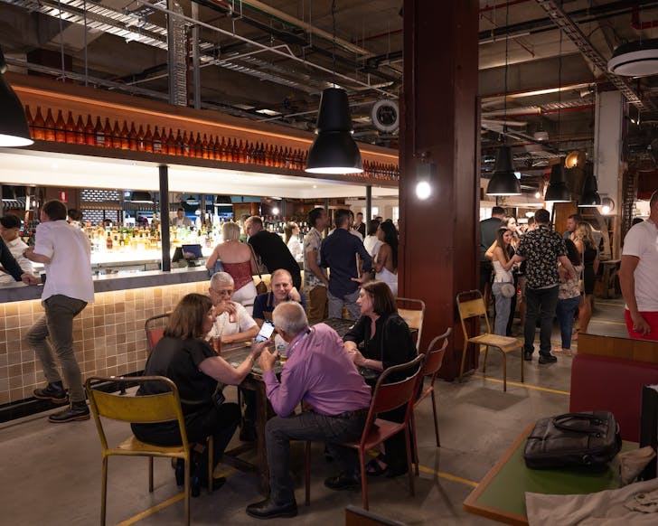 people sit at tables and stand at the bar inside hay st market in sydney