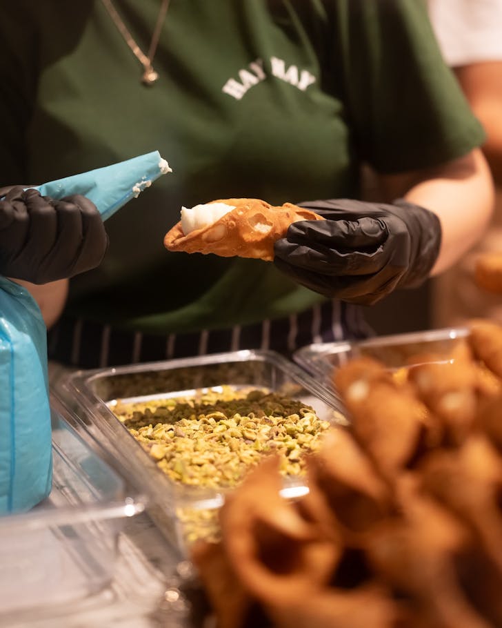 a pastry chef pipes a fresh cannoli at hay st market