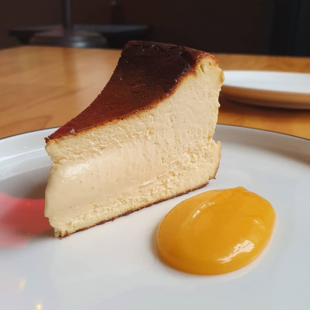 a slice of basque cheesecake on a plate with a yellow yuzu curd