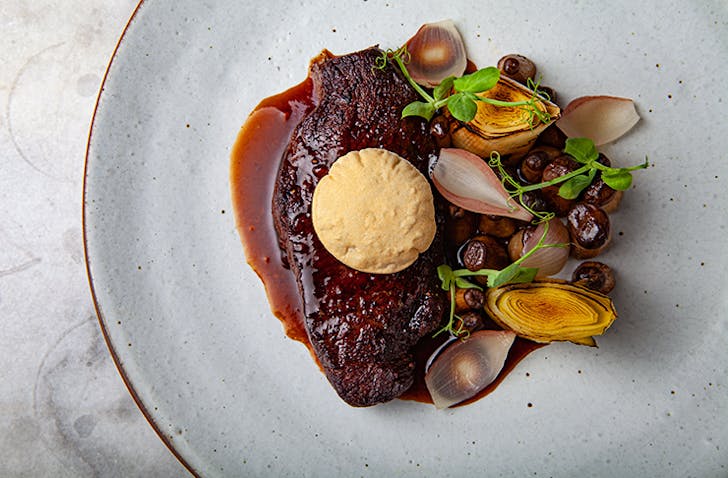 A rich rump cap steak covered in gravy on a stone-like plate.