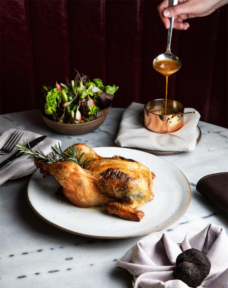A fresh-roasted chicken next to a truffle in a hand-towel.