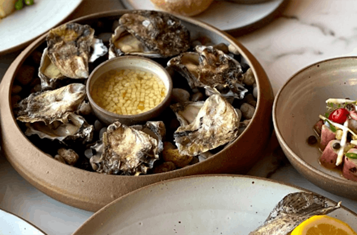 A plate of Sydney Rock oysters with a small bowl of apple vinaigrette in the centre.