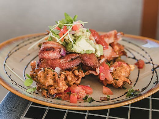 Corn fritters on a plate with smashed avo, salsa and bacon